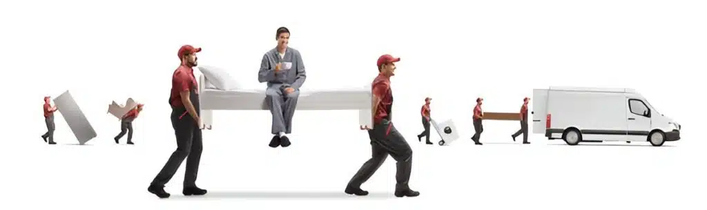Two cheerful local movers in red caps and uniforms carefully carry a bed with a man sitting comfortably on top, sipping from a mug. Other movers transport boxes and appliances nearby, all heading towards a white moving van. This depicts a seamless and efficient moving process.