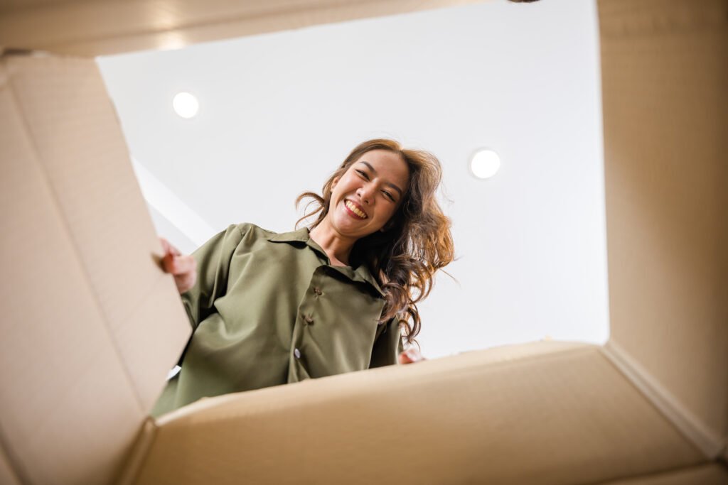 Self storage Castlebridge - Blackwater | Trusted Local Self storage 7 A smiling woman unpacks a cardboard box, her joyful expression suggesting a positive moving experience. She wears a green shirt in a bright, homey setting. Local movers make moving day easier!