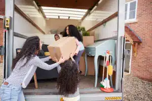 Mother And Children Unloading Furniture From Removal Truck Into New Home