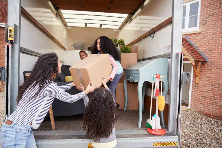 Mother And Children Unloading Furniture From Removal Truck Into New Home