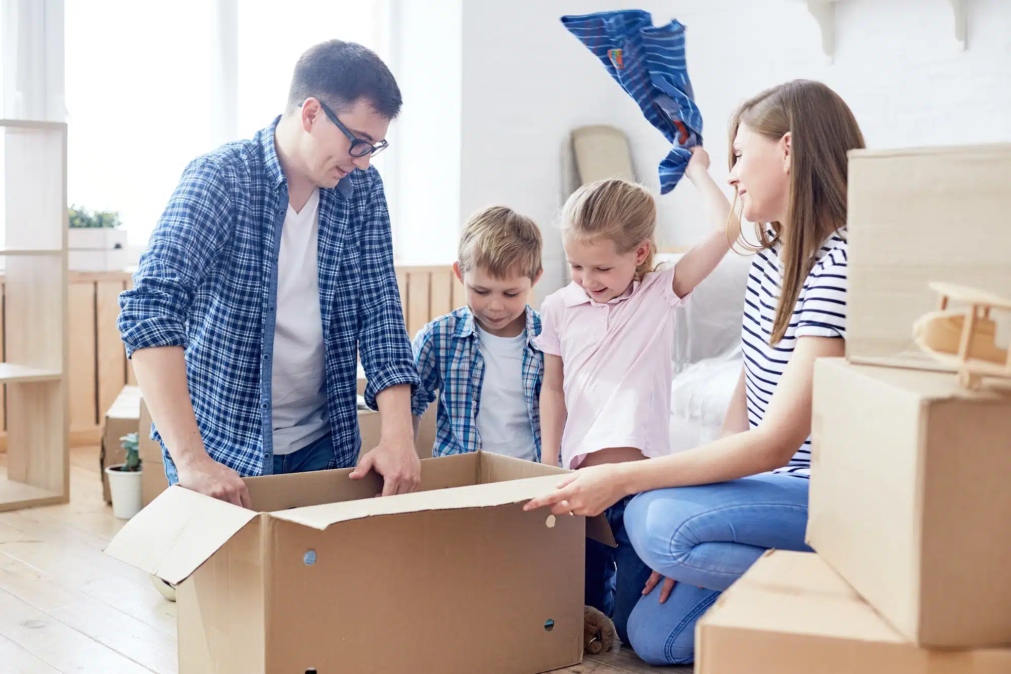 Happy family unpacking boxes in their new home, parents helping children unpack clothes. The children are excited, and the parents look content and joyful. Moving day excitement!