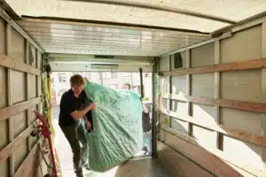 Removals business. A man lifting an item of furniture covered in green plastic into a removals van. ,Moving Home with Removals Company,Ireland