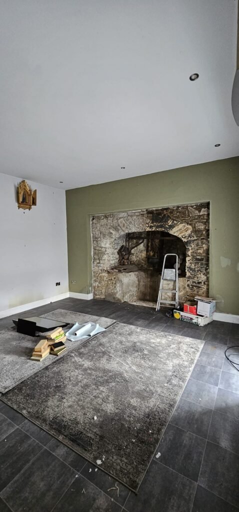 Renovation in progress: A rustic stone fireplace is exposed in a room with green walls, tools, and rolled-up wallpaper, hinting at a house relocation project.