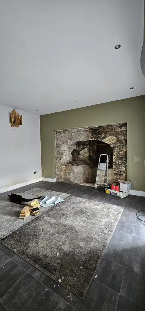 Renovation in progress: A rustic stone fireplace is exposed in a room with green walls, tools, and rolled-up wallpaper, hinting at a house relocation project.