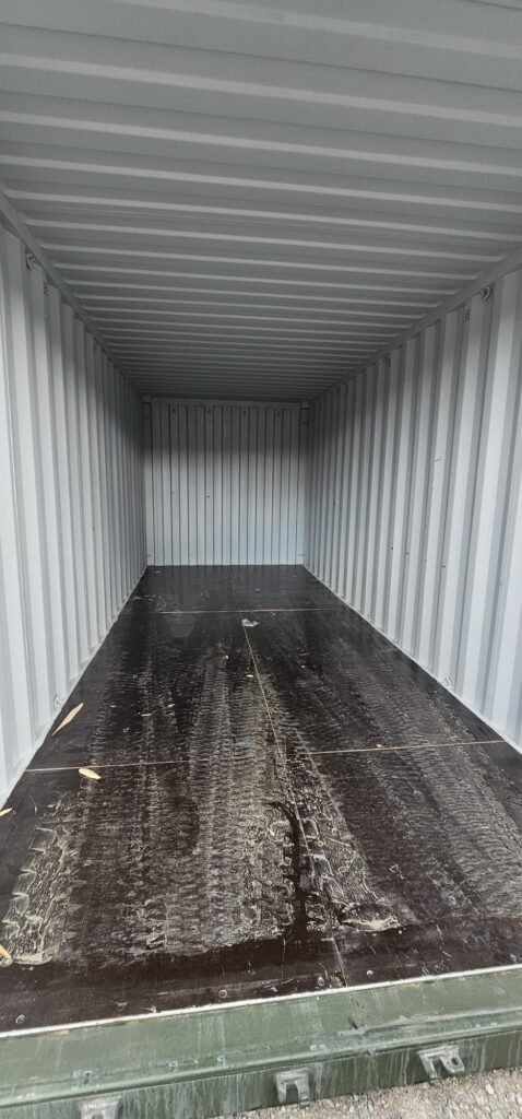 Interior of an empty shipping container with a dark, worn wooden floor, ready for moving household items.