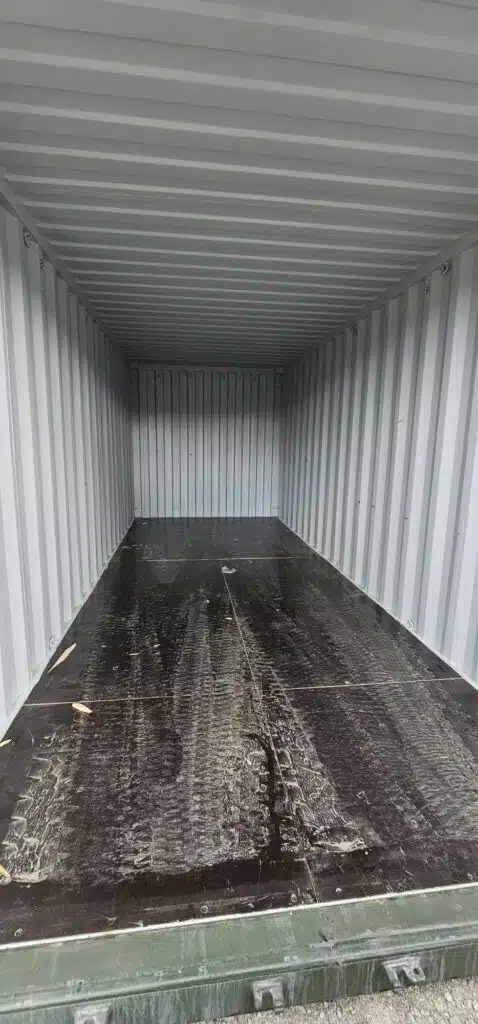 Interior of an empty shipping container with a dark, worn wooden floor, ready for moving household items.