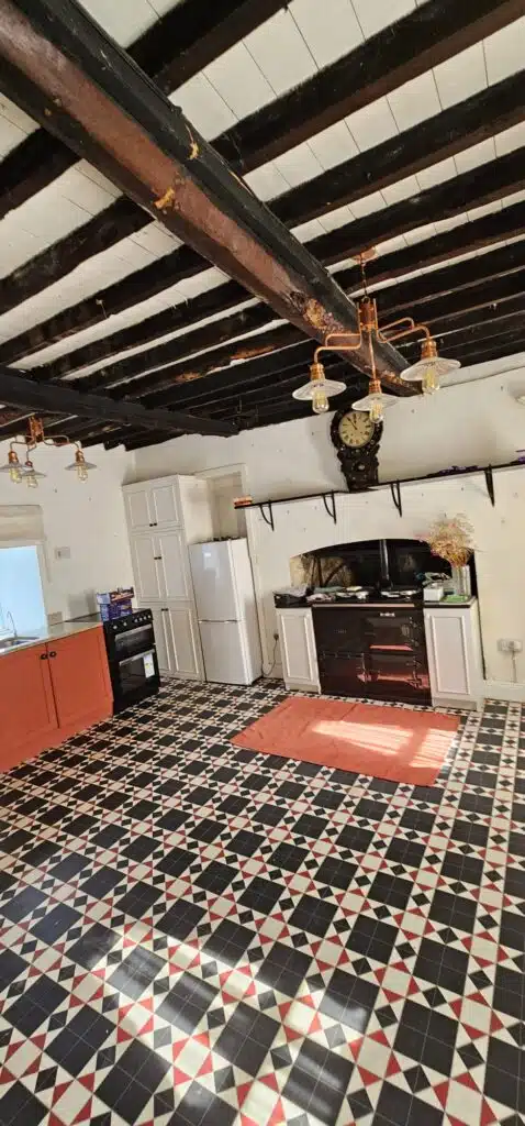 Rustic kitchen with black and white geometric floor tiles, an Aga stove, and exposed wooden ceiling beams, reminiscent of a house featured in the Irish Independent.