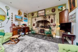 Cozy living room with a large stone fireplace, antique furniture, and green armchairs, reminiscent of a house featured in the Irish Independent.