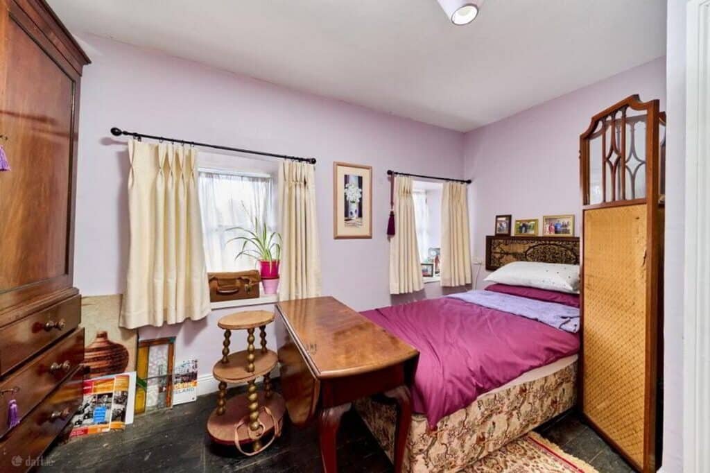 A cozy bedroom with a single bed, antique wooden furniture, and pale lavender walls, possibly from a house featured in an Irish Independent case study.