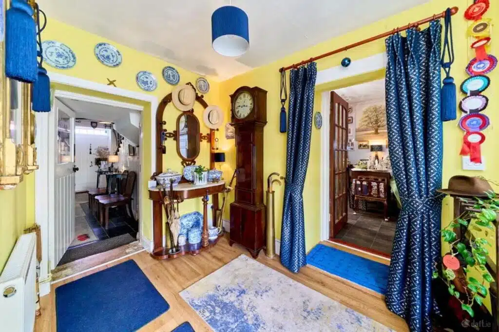 Bright yellow hallway with blue accents, featuring a grandfather clock, decorative plates, and a hat stand, as seen in a case study about local movers.