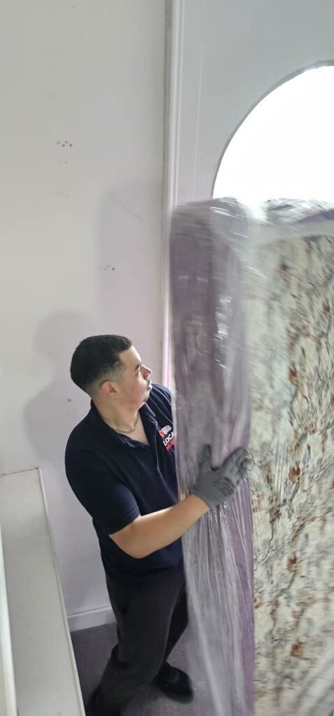 Man in blue shirt and gloves moving a wrapped mattress