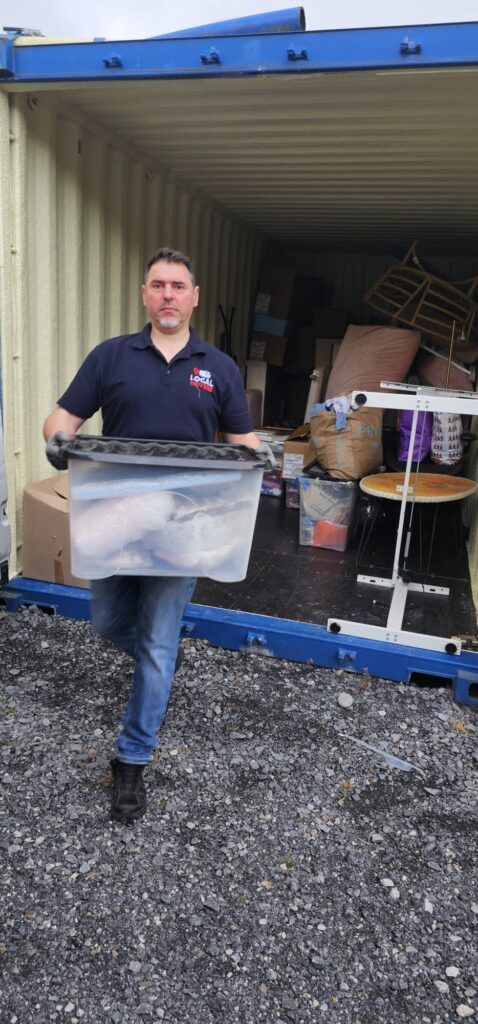 Man carrying a clear plastic bin filled with items into a shipping container, likely part of a move from Dublin to Sligo.