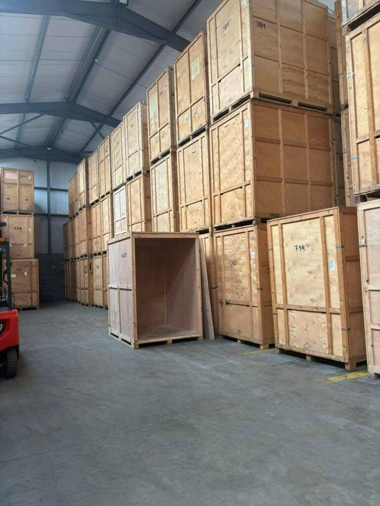 Rows of large wooden storage crates stacked high inside a warehouse, possibly used for moving from Dublin to Sligo. Some crates have numbers like '381' and '714' visible.