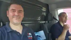 Two Local Movers employees in uniform, one smiling and the other giving a thumbs up, sit inside a moving van during a commercial relocation.