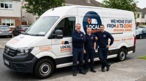 Three smiling local movers stand proudly in front of their white branded van, which displays "Local Movers" and "We Move Stuff From A to Done Affordably. Reliably.